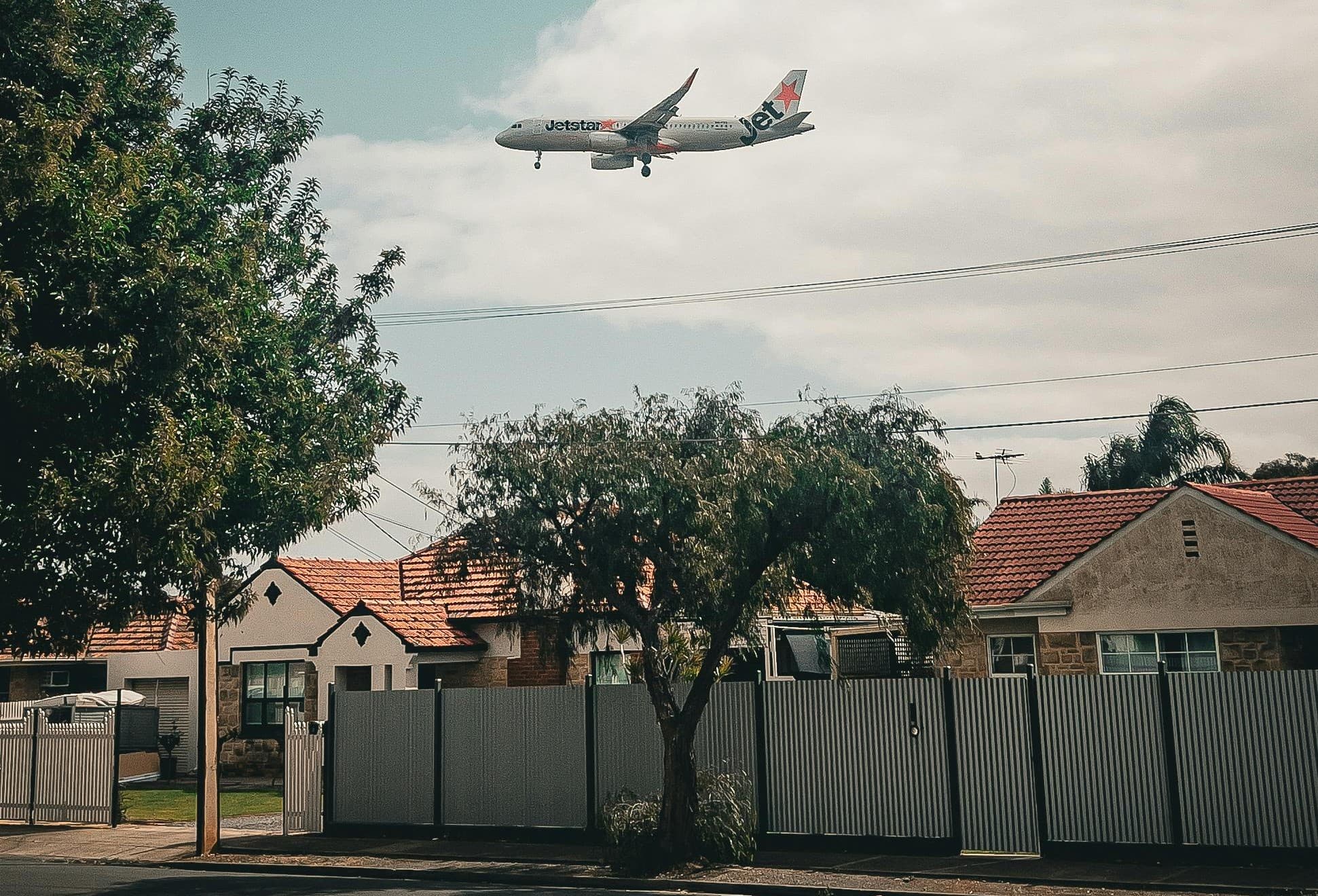 A passenger jet on final approach passing low over the rooftops of an Australian suburb on a clear day
